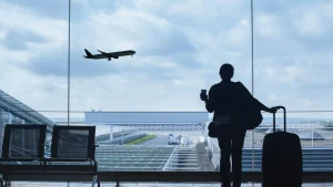 Silhouette of a business traveler with luggage looking out an airport window at a departing plane, representing seamless corporate travel management in Ghana.