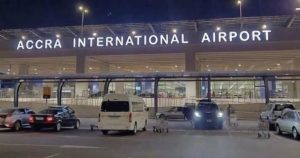 Night view of the illuminated "ACCRA INTERNATIONAL AIRPORT" main terminal exterior and entrance parking lot, highlighting the primary aviation hub funded by Ghana's new airport infrastructure levy.