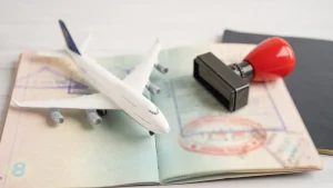 A toy airplane resting on an open passport filled with official immigration stamps next to a rubber stamp tool, highlighting the travel choices between a single entry vs multiple entry visa.
